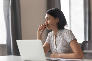 A young woman sitting down, procrastinating working on her laptop. Representing how anxiety can often exasperate the procrastination cycle. Learn how to beat it today in anxiety therapy in NYC, NY. 