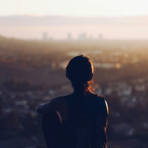 An individual sitting on an edge, looking at a skyline of a city. Gold Therapy NYC is here to help you! We offer anxiety counseling in NYC.