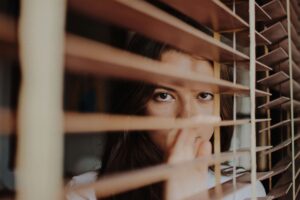 A women peeking through the blinds. With anxiety counseling in NYC, NY, you can heal your health anxiety! Get started with anxiety therapy today. 
