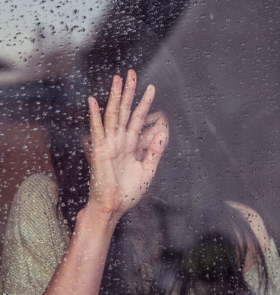A woman setting her hand on a window with raindrops. If you want to discover the root cause of your anxiety, get started with anxiety therapy in NYC, NY today. Our anxiety therapists are ready to help you.