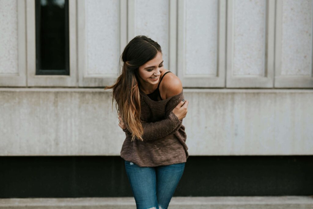 A young woman laughing while hugging herself. Representing how anxiety therapy in NYC can help you grow self compassion. Begin working with an anxiety therapist now!