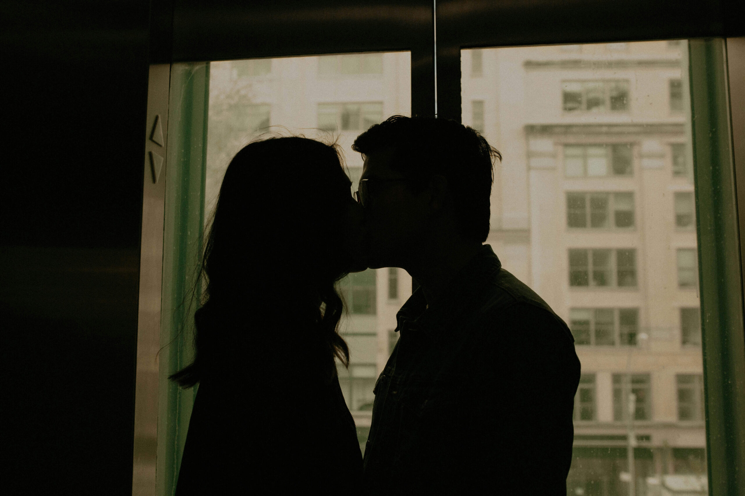 A couple kissing in front of a window. If you can feel anxiety rising in your relationship, reach out to us. We offer therapy for anxiety in NYC!