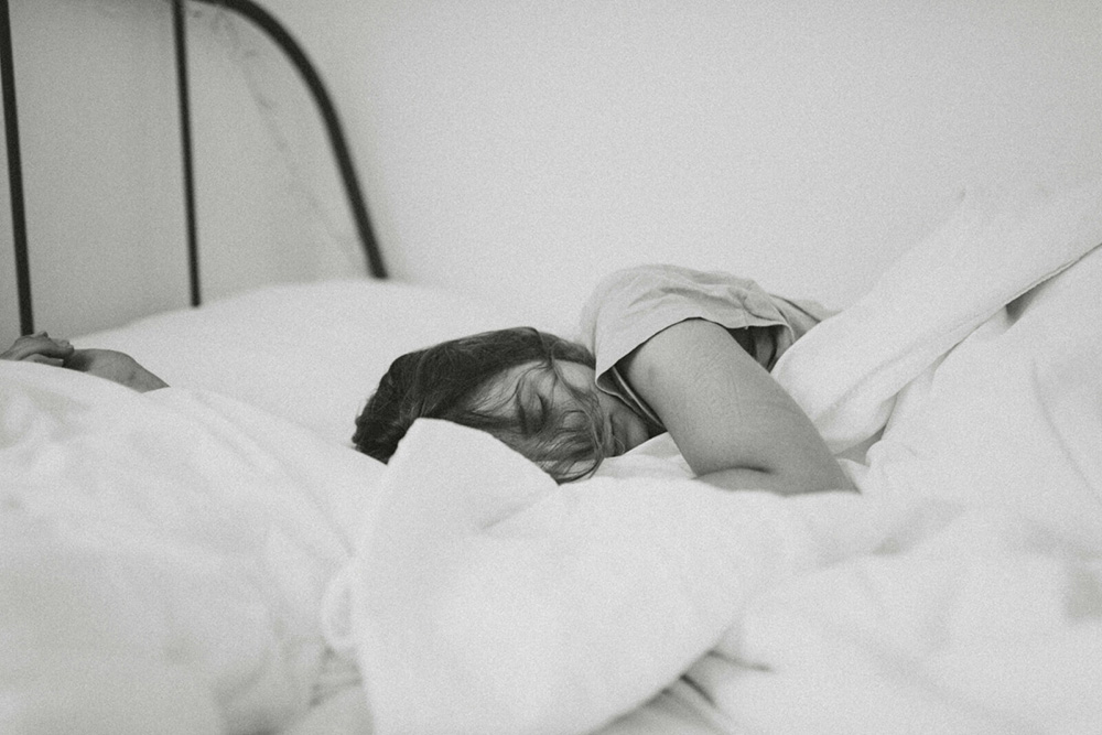 A young adult laying in bed with her eyes closed. With an anxiety therapist in NYC, NY, you can discover stress management skills. We offer anxiety counseling to help. 