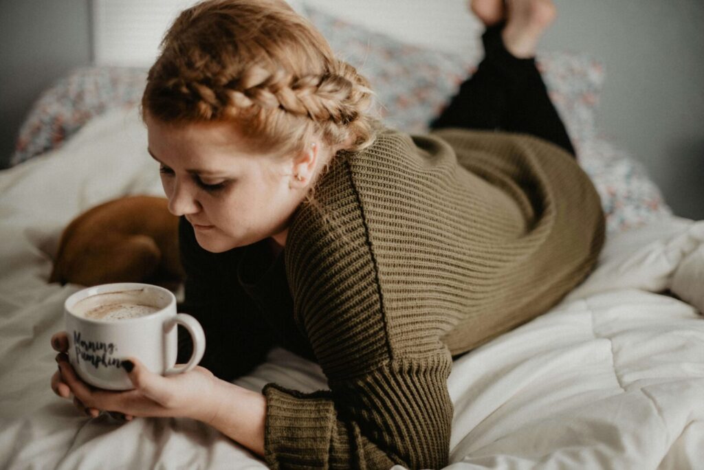 A young woman holding a cup of coffee while laying bed. In anxiety therapy in NYC, NY, you can develop coping strategies for your anxiety. Call me today to begin anxiety counseling!