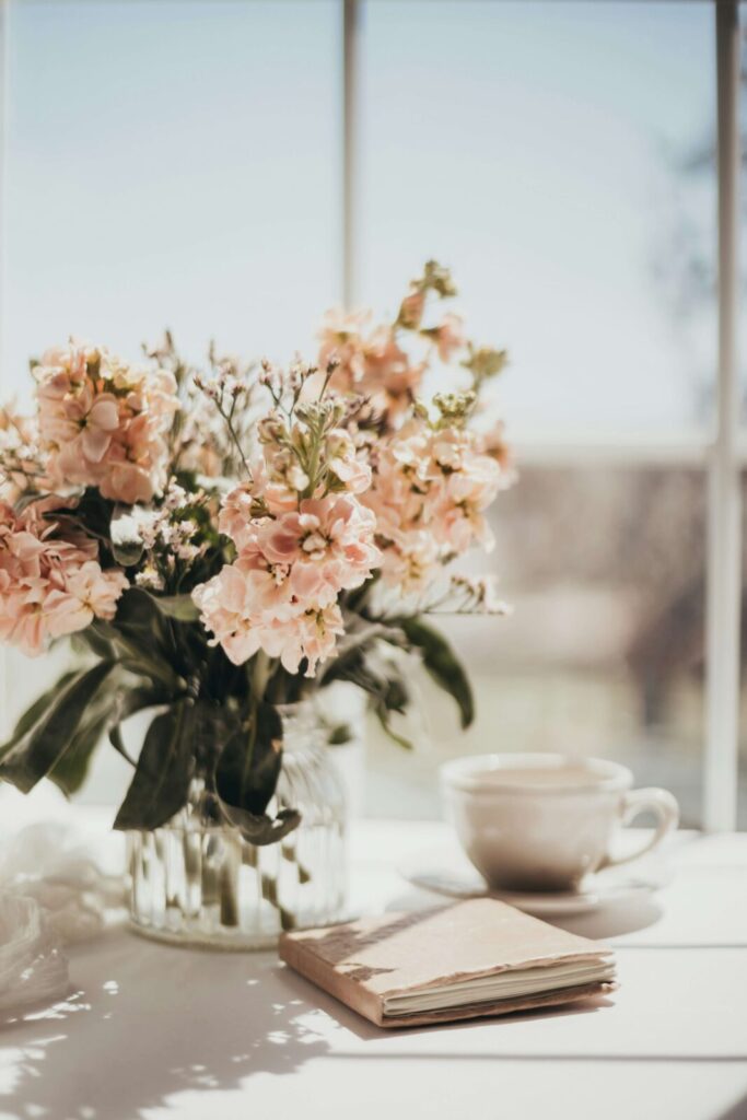 Pink flowers by a mug & journal. Representing how journaling can relieve anxiety symptoms. Learn more in anxiety counseling in NYC, NY.