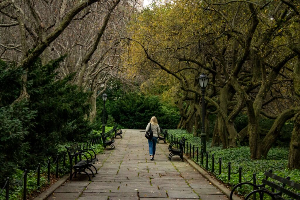 A woman walking through a park alone. Representing how anxiety can cause loneliness & self-doubt. Work with an anxiety therapist in NYC, NY to manage your anxiety! 