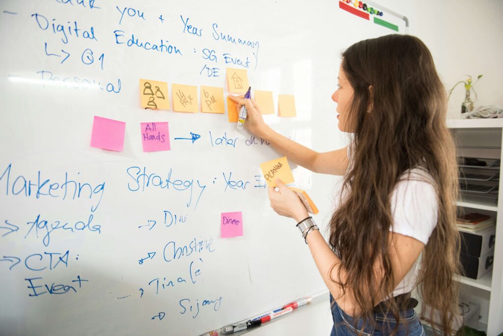 A young professional women working on a whiteboard with sticky notes. Our anxiety therapy in NYC can help you manage your anxiety! With the help of an anxiety therapist, you can tackle anything! 