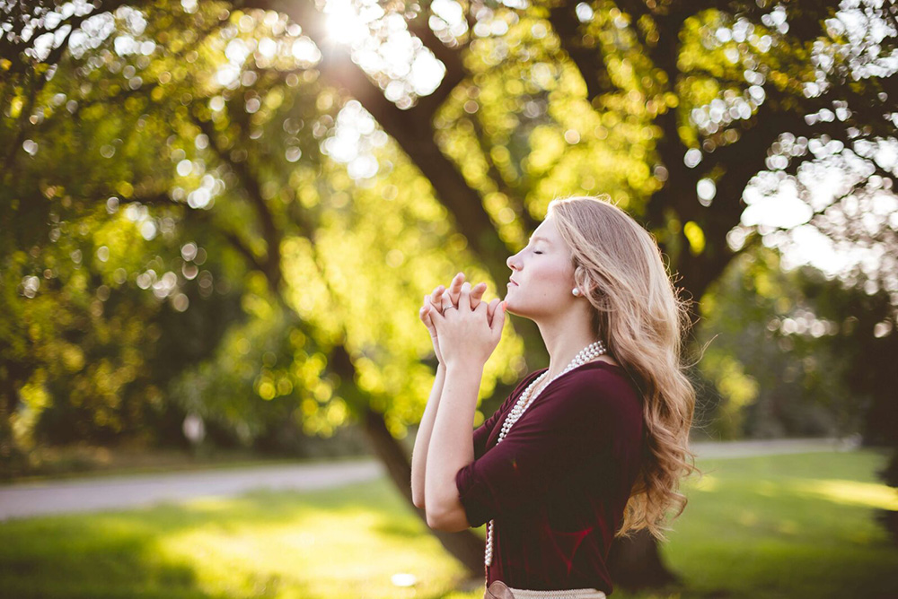 A woman holding her hands together and taking a deep breathe outside. If you want to learn more about self-compassion, start working with an anxiety therapist in NYC, NY. Call today to start practicing self-compassion.