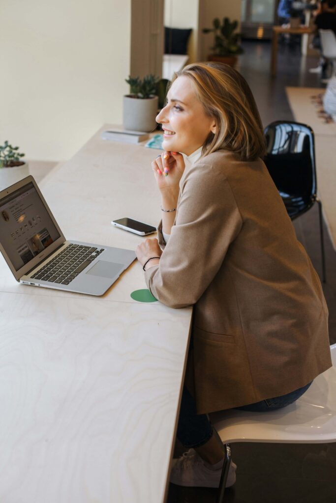 A woman smiling while sitting at a desk with a laptop & phone. Anxiety counseling in NYC is a safe place to explore work stress & anxiety. Start working with an anxiety therapist today.