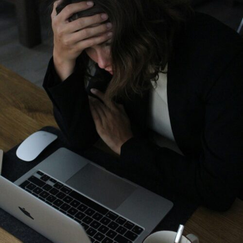 A woman holding her head while looking at her laptop. Representing how work anxiety can feel overwhelming. Start working with an anxiety therapist in NYC, NY to help!