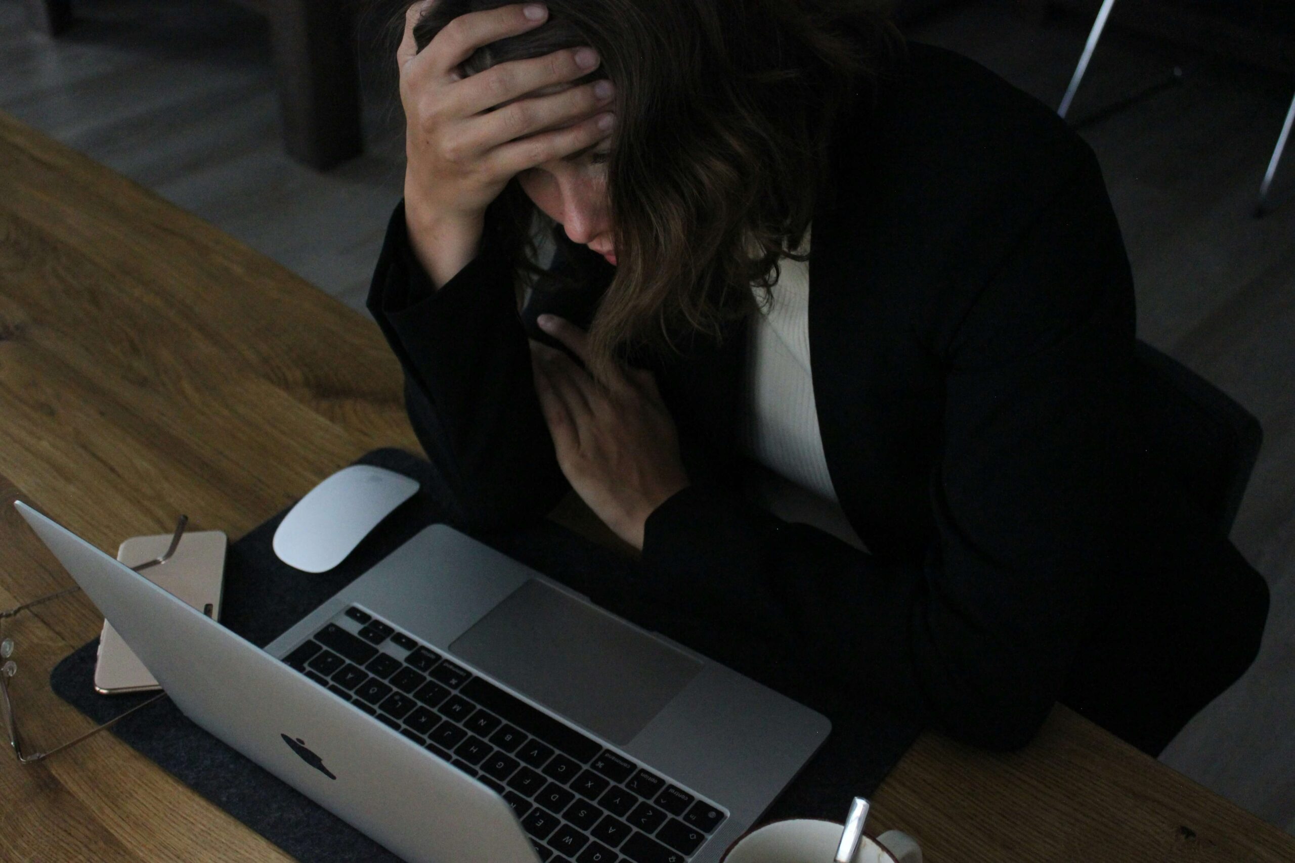 A woman holding her head while looking at her laptop. Representing how work anxiety can feel overwhelming. Start working with an anxiety therapist in NYC, NY to help!
