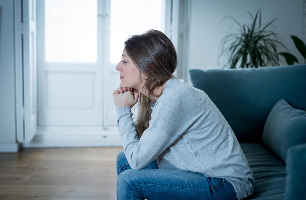 A woman sitting on a couch while resting her elbows on her knees. This represents how retroactive jealousy may feel overwhelming. In anxiety counseling in NYC, NY, we can help you!