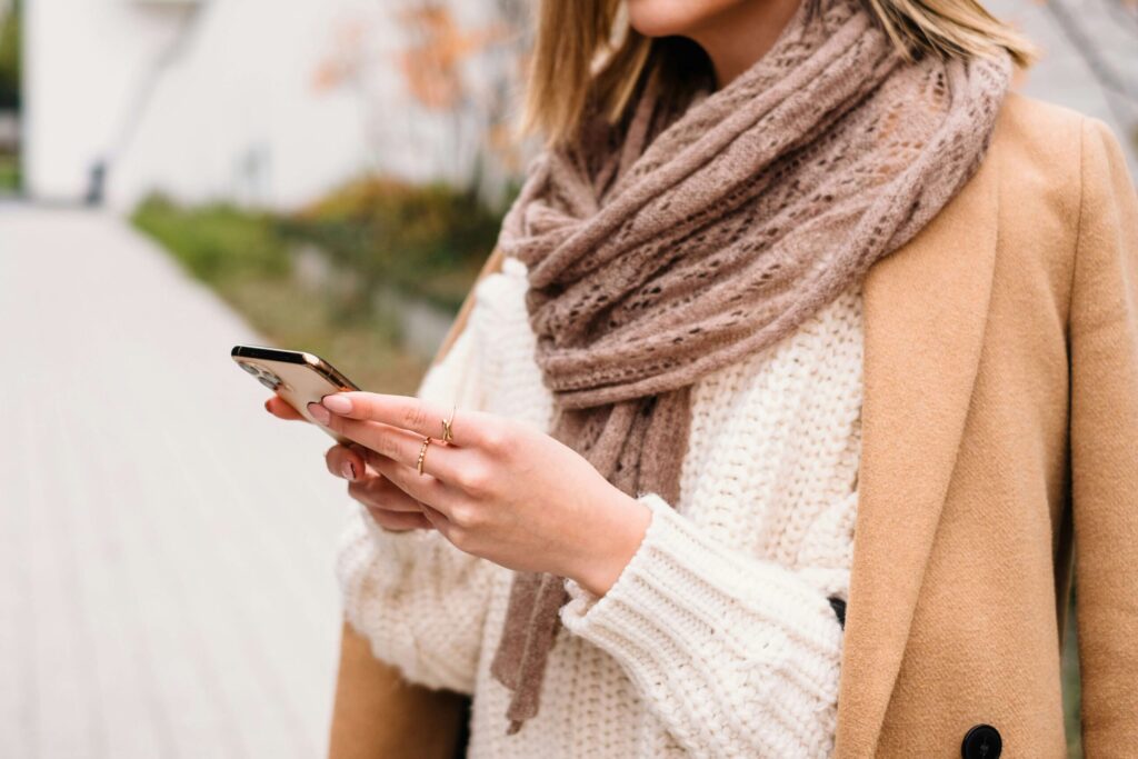 A woman standing while looking at her Iphone. Representing how retroactive jealousy in relationships may look like checking your partners social media often. Get started with an anxiety therapist in NYC, NY to help!