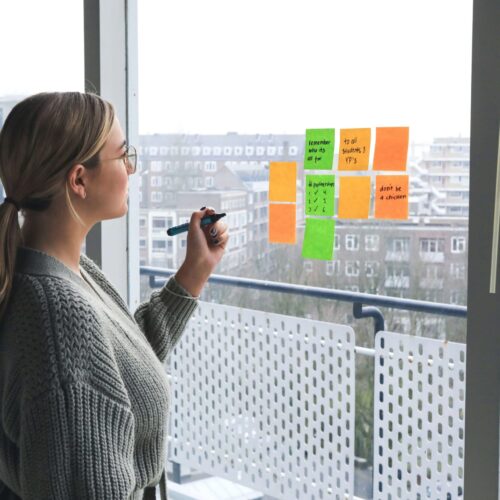 A woman sticking sticky notes on the window while writing on them. This represents how the past paced NYC lifestyle may cause work anxiety. Start working with an anxiety therapist in NYC, NY today.