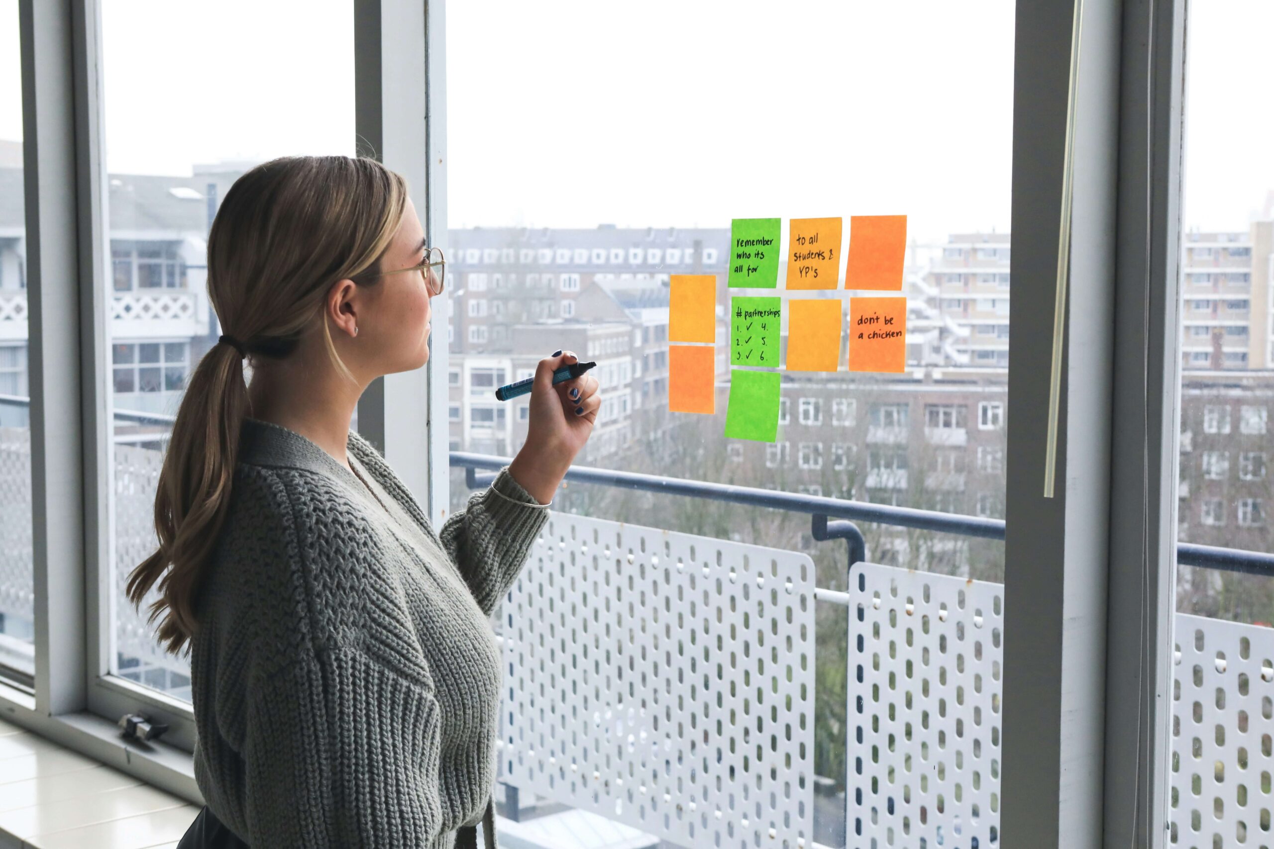 A woman sticking sticky notes on the window while writing on them. This represents how the past paced NYC lifestyle may cause work anxiety. Start working with an anxiety therapist in NYC, NY today.
