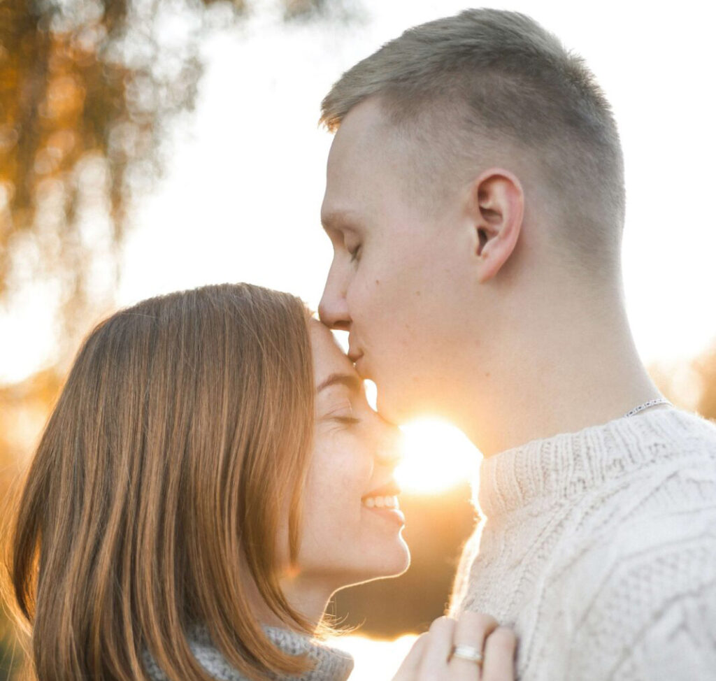 A man kissing a woman's forehead during a sunset. Anxiety counseling in NYC, NY can help your ROCD & anxious attachment. Start your recovery journey today!