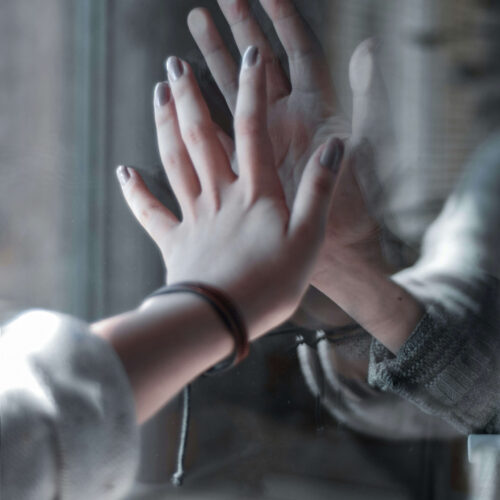 A woman reaching out to a window meeting someone on the other side also reaching out. If you want to learn how to manage your attachment style better, anxiety counseling in NYC can help! Call now to begin.