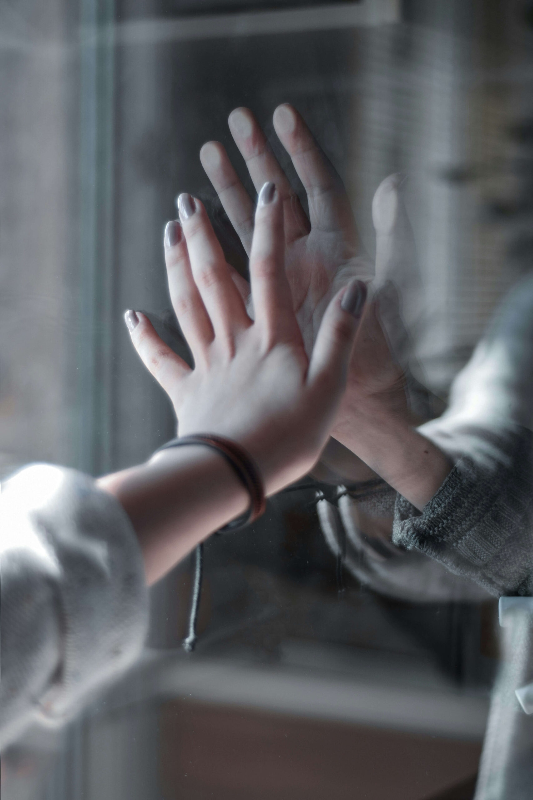 A woman reaching out to a window meeting someone on the other side also reaching out. If you want to learn how to manage your attachment style better, anxiety counseling in NYC can help! Call now to begin.
