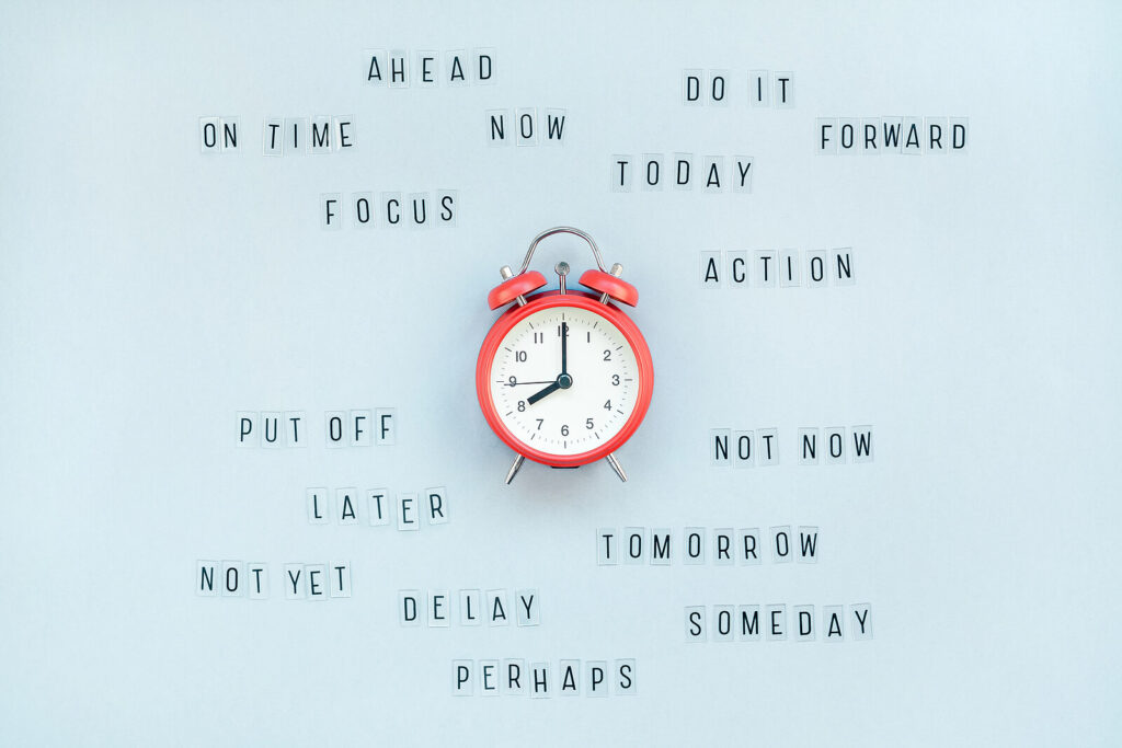 A red clock on a blue background surrounded with words like "ahead", "action", focus". Representing how you can explore procrastinations root causes in anxiety counseling in NYC, NY. Get started today!