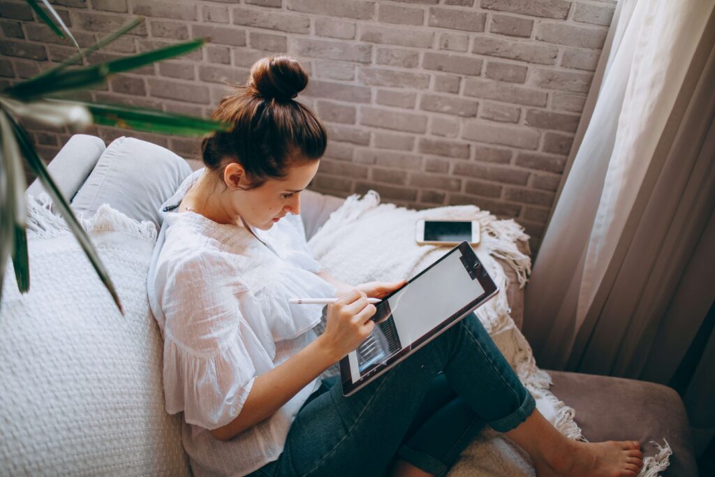 A young women working on her iPad while sitting on a couch. Anxiety therapy in New York City, NY can uncover the roots of your procrastination. Uncover them today with an anxiety therapist. 