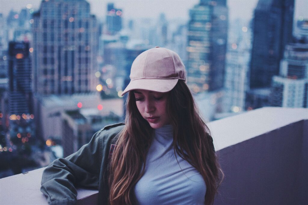 A woman wearing a baseball hat standing in front of a NY skyline view. Discover how anxiety counseling in NYC can help you find balance in your life. Start your healing journey today. 