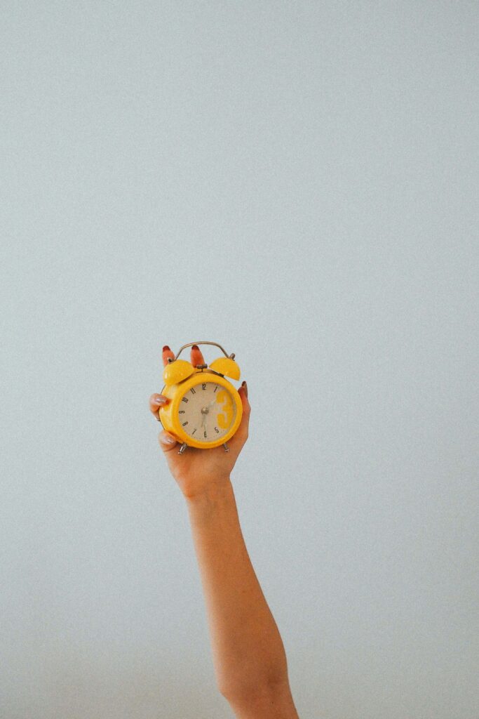 A woman with red nails holding up a yellow clock in the air. Anxiety & procrastination can go hand-in-hand. Discover how to beat the cycle in anxiety therapy in NYC, NY. 